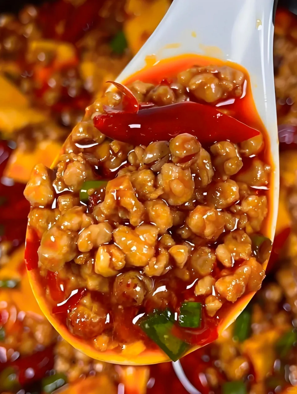 Spoon of dandan noodles topped with crispy minced pork in chili oil